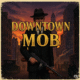 A menacing gangster from a 1930s Mafia game stands in a shadowy downtown street with a tommy gun.